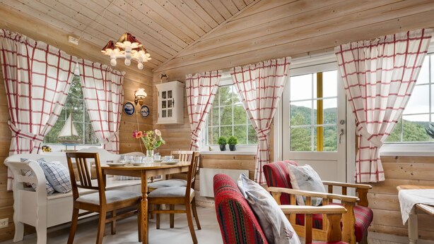 L’intérieur d’un chalet accueillant, avec une table à manger en bois, des chaises, un canapé et une fenêtre agrémentée de rideaux.