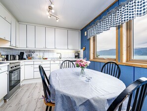 A modern kitchen with white cabinets, a dining table with a vase of flowers, and a window with a view of mountains. - Hovsfjellet by Interhome (Fresvik)