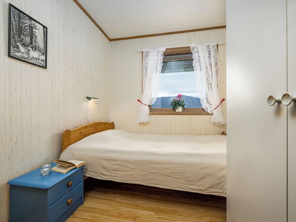 A bedroom with a bed, a nightstand, a window with a view, and a wall-mounted light.