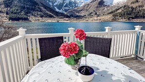 Ein Tisch mit weißer Tischdecke und einer Vase roter Blumen, mit Blick auf einen See und Berge im Hintergrund.