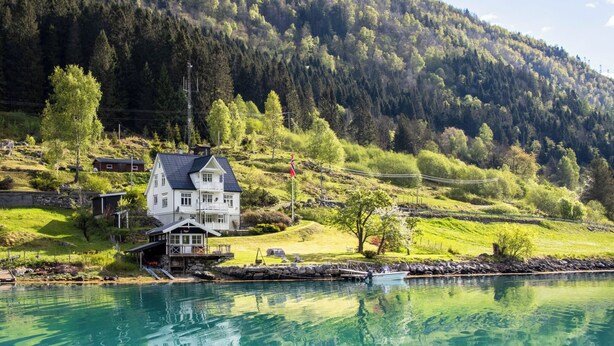 Ein Haus am See mit einer Anlegestelle, umgeben von Grünflächen und Hügeln.