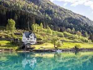 A lakeside house with a dock, surrounded by lush greenery and a forested hillside.