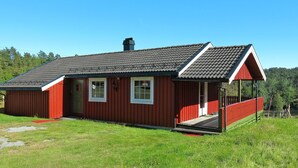 A red wooden house with a sloped roof, a chimney, and a porch with a red railing.