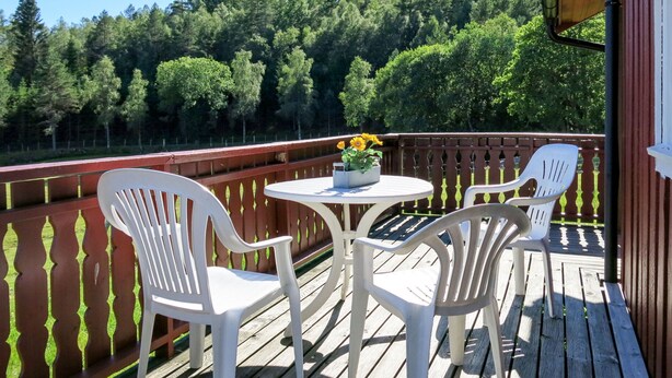 A wooden deck with two white plastic chairs and a small round table with a flower pot.