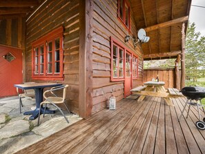 Eine Holzhütte mit Veranda, einem Esstisch, Stühlen, einem Grill und einer Satellitenschüssel.