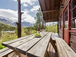 Ein Holztisch mit einer Weinflasche, Gläsern und einer Schale Trauben auf einer Terrasse mit Blick auf eine Berglandschaft.