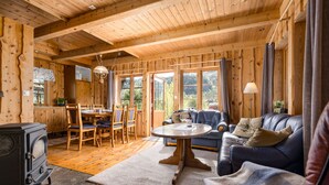 Een knus houten blokhutinterieur met een eethoek, een bank en een houtkachel.