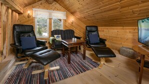Een gezellig vakantiehuisje met houten wanden en plafond, met twee leren fauteuils, een kleine tafel en een televisie.