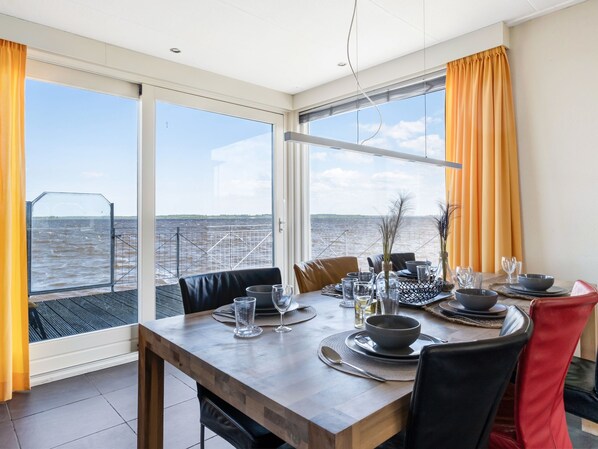 A dining area with a table set for four, large windows with curtains, and a view of the water.