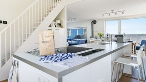 A modern kitchen with a central island, a dining area with a bar, and a staircase leading to an upper level.