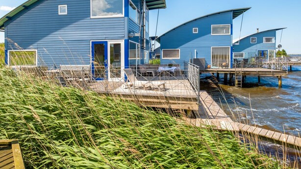 A blue waterfront house with a deck and a dock extending into the water.