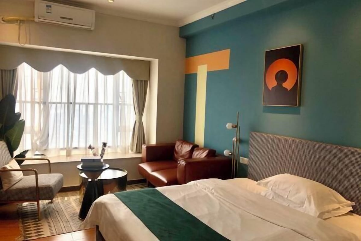 Quarto de hotel com cama, sofá, uma mesinha e janela com cortinas.