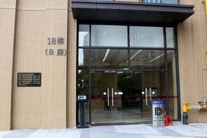 Entrada de um edifício com porta de vidro, hidrante e placa com caracteres japoneses.