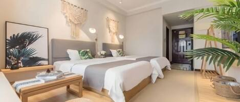 A modern hotel room with a large bed, bedside tables, a small seating area, and a potted plant.