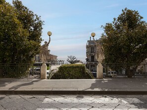 Un chemin pavé, avec une statue de chaque côté, bordé d’arbres et d’une clôture en métal.