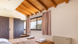 Quarto com teto de madeira, cama com cobertor marrom, janela com cortinas e radiador.