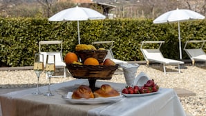 Uma mesa com comida e bebidas, cadeiras para área externa e vista para uma montanha.