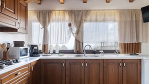 Uma cozinha com armários de madeira, micro-ondas, pia e janela com cortinas.