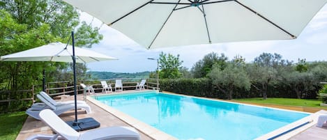 A swimming pool with lounge chairs and umbrellas, surrounded by a wooden deck and greenery.
