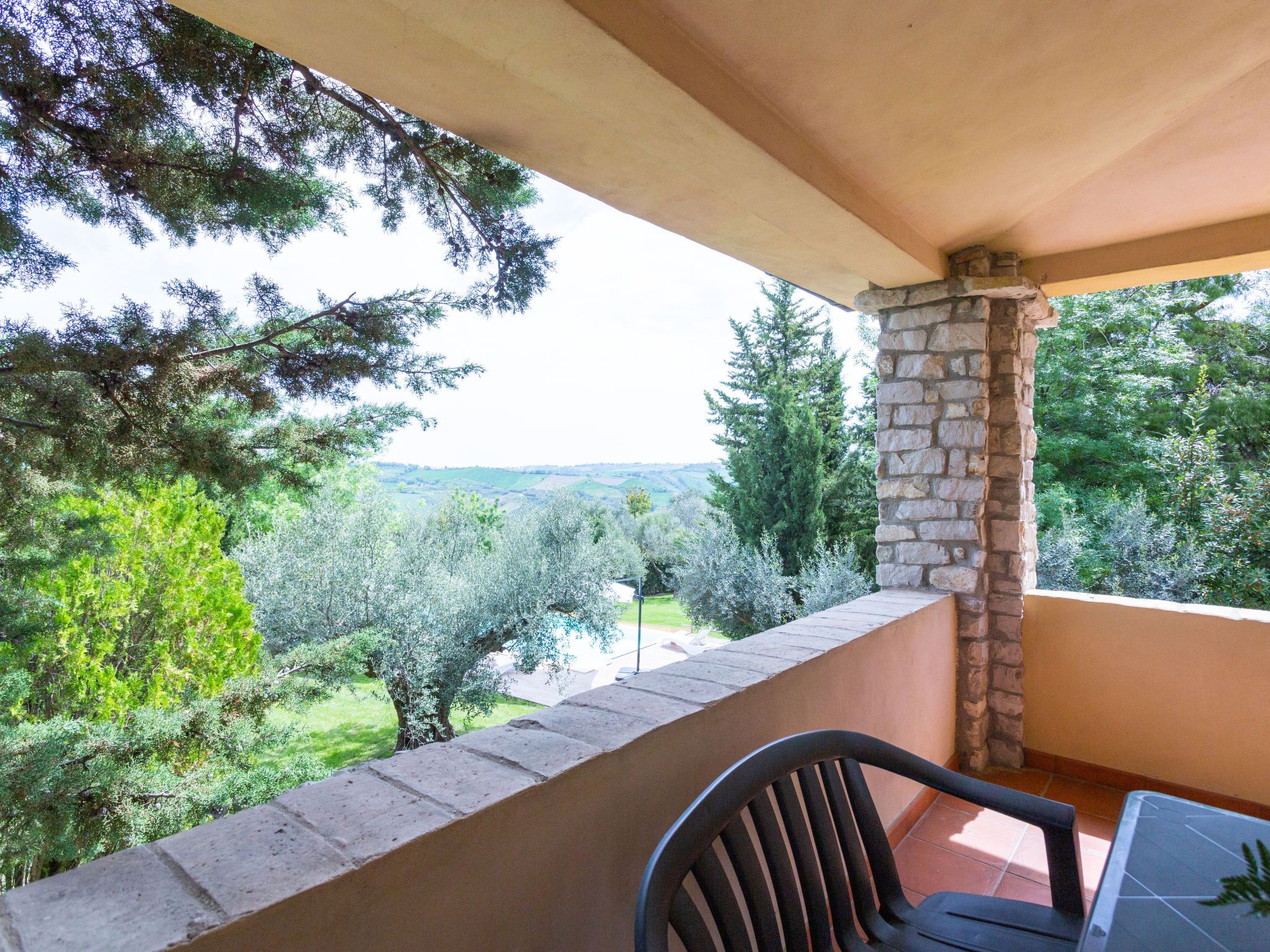 A balcony with a stone pillar, a black chair, and a table.