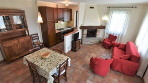 A cozy living room with a fireplace, a dining area with a table and chairs, and a kitchen with wooden cabinets and a stove. - La Corte Bricca (Bilo A) by Interhome (Oltrepò Pavese)