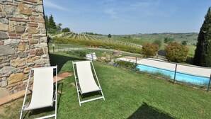 A poolside area with two lounge chairs, a stone wall, and a view of vineyards and hills. - La Corte Bricca (Bilo A) by Interhome (Oltrepò Pavese)