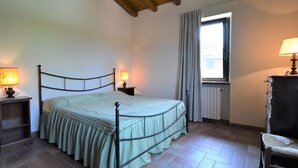 A bedroom with a bed, two bedside lamps, a window with curtains, a radiator, and a chair. - La Corte Bricca (Bilo D) by Interhome (Oltrepò Pavese)