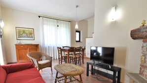 A living room with a red sofa, wicker chairs, a dining table with chairs, a television on a stand, and a stone fireplace. - La Corte Bricca (Bilo D) by Interhome (Oltrepò Pavese)