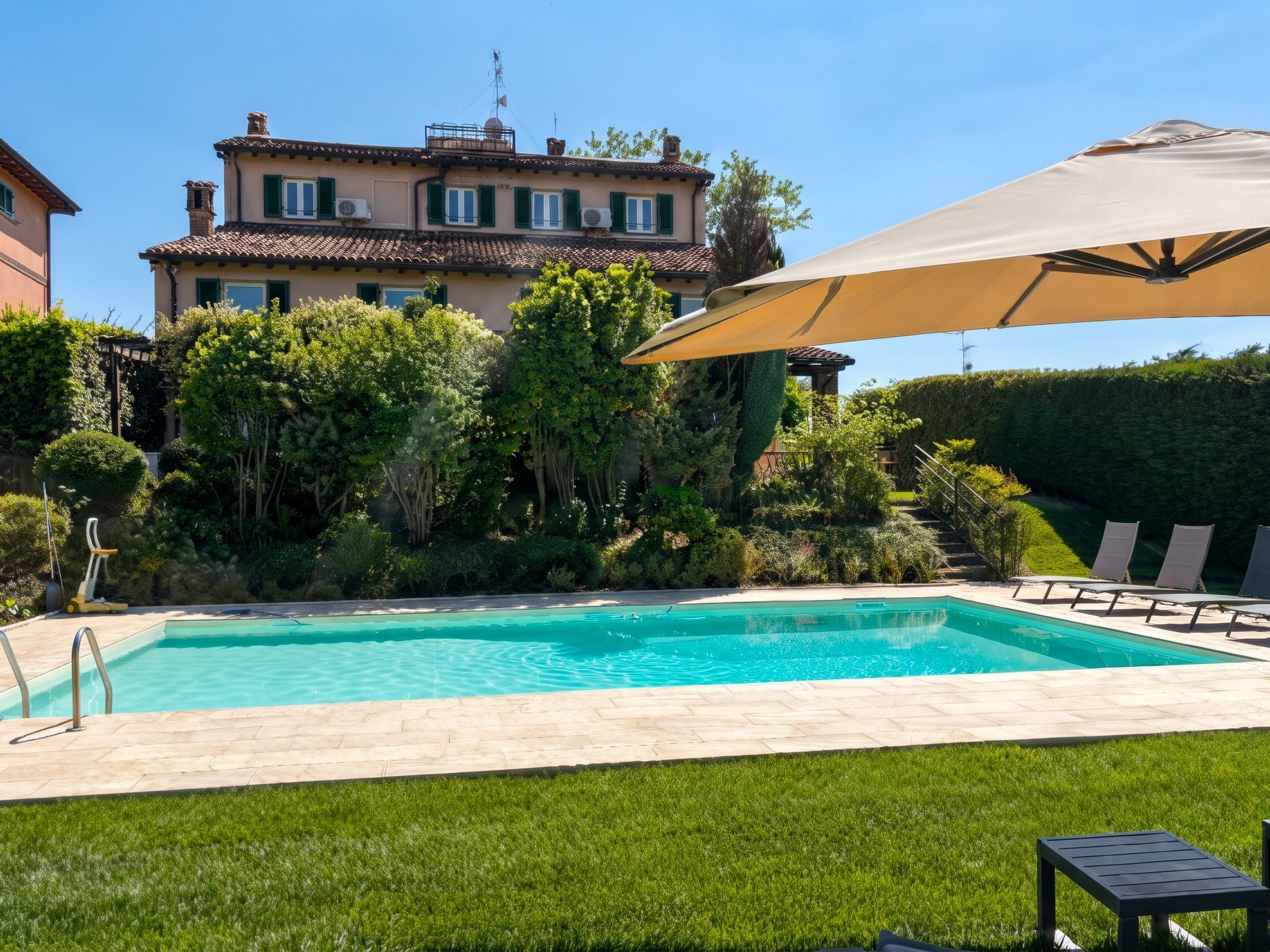 A swimming pool with a clear blue water, surrounded by a well-maintained lawn and a large house in the background.