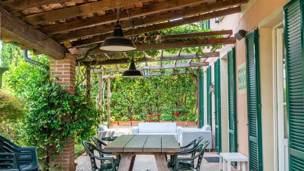 An outdoor patio with a wooden pergola, green chairs, a table, and a white sofa. - Ca' del Vento by Interhome (Oltrepò Pavese)
