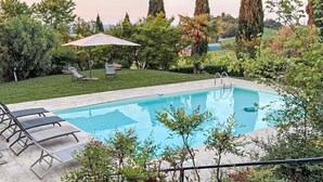 A swimming pool with lounge chairs, surrounded by greenery and tall trees. - Ca' del Vento by Interhome (Oltrepò Pavese)