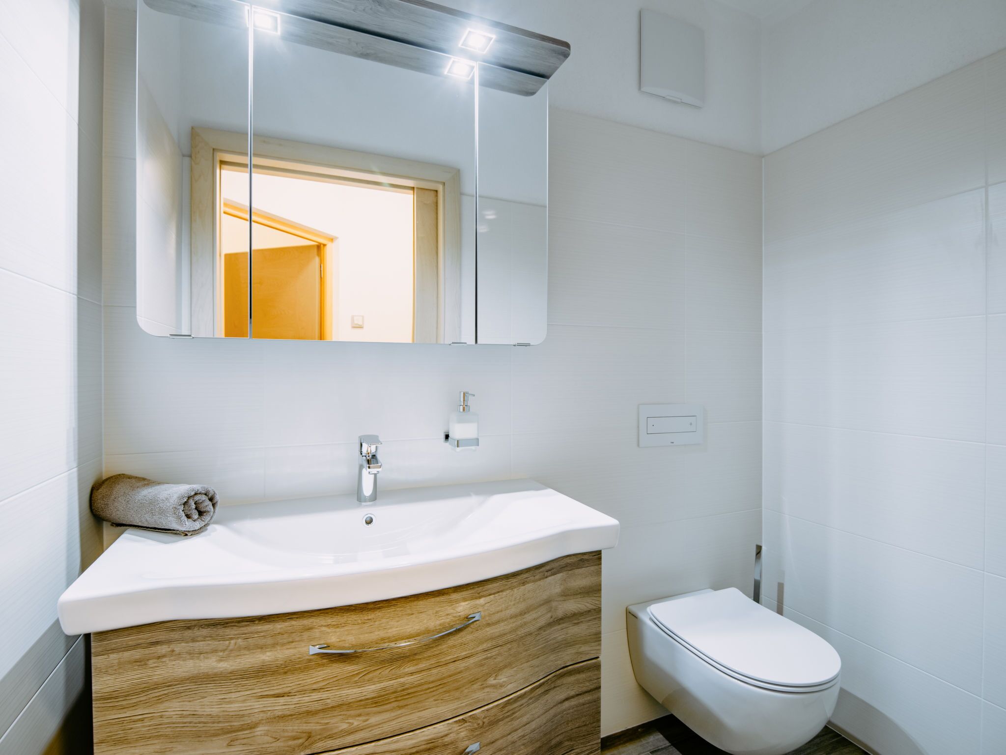 Une salle de bain moderne avec un meuble-lavabo blanc, un meuble en bois et des toilettes blanches.