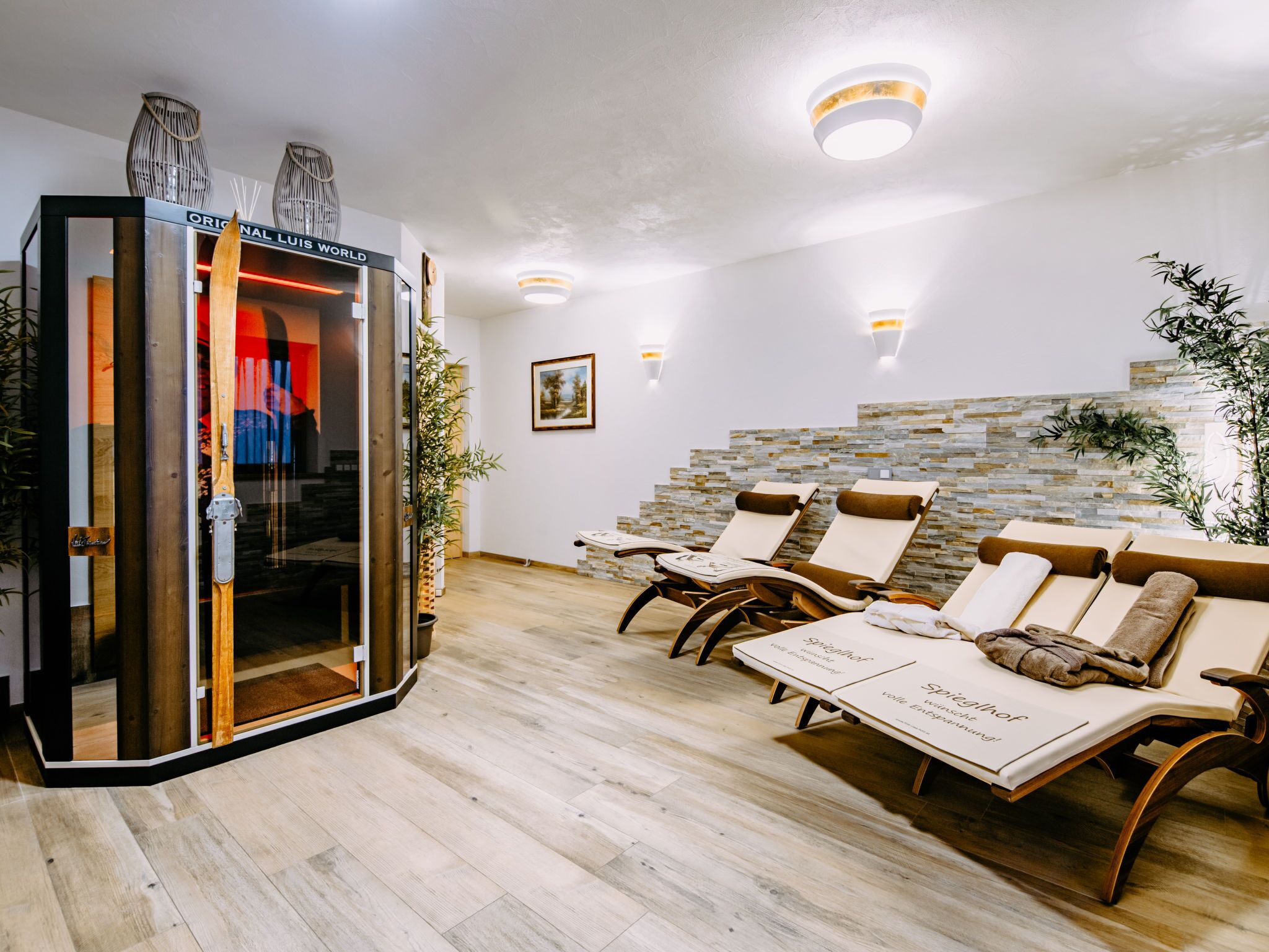 A spa area with wooden flooring, stone wall, and lounge chairs with towels.