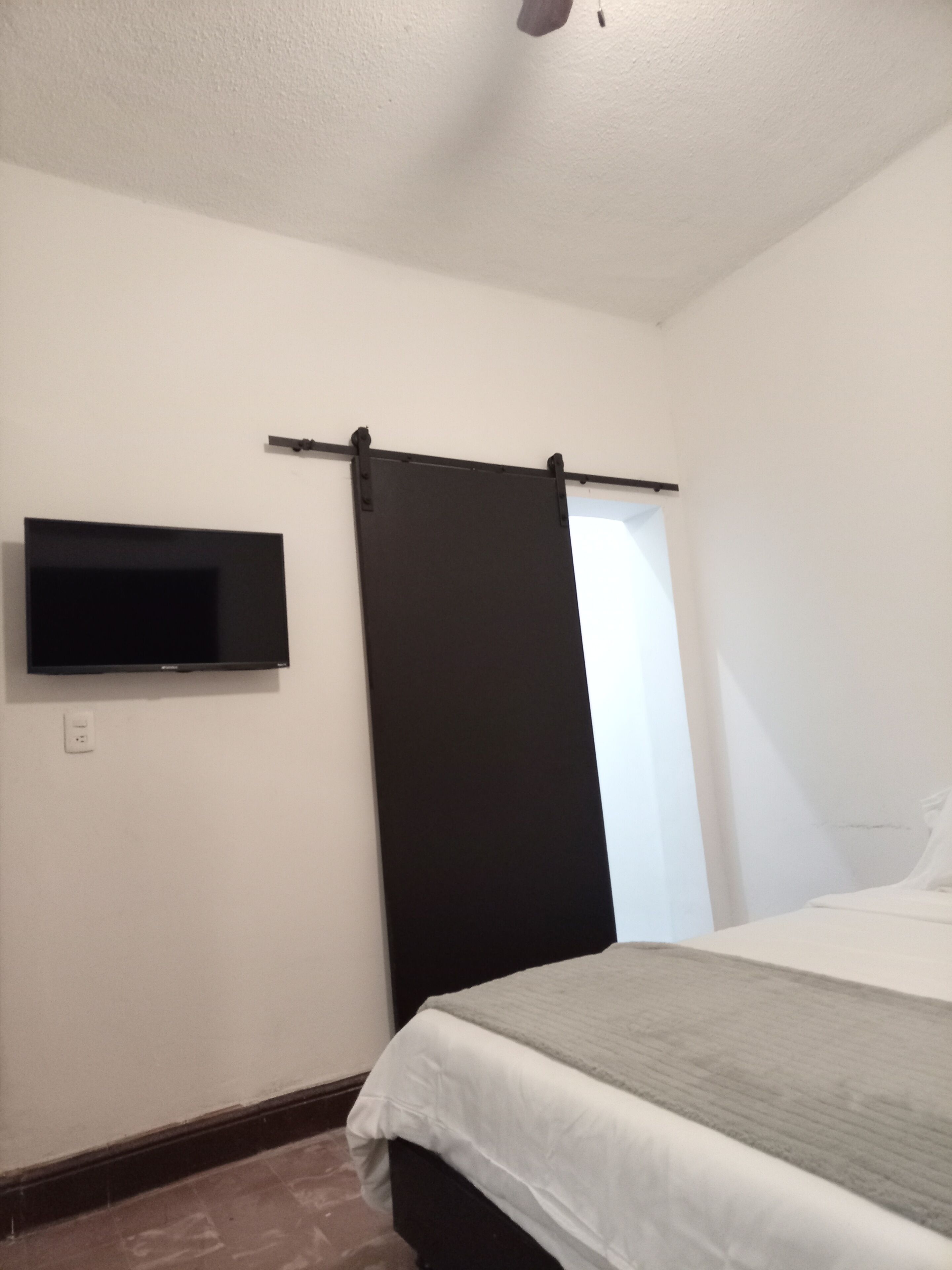 Un dormitorio con cama, televisor de pantalla plana en la pared y puerta corredera.