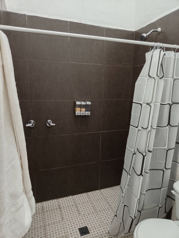 Un baño con ducha, paredes de azulejos oscuros, un inodoro blanco y un perchero para toallas.