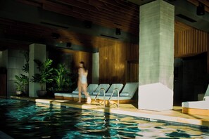 Una piscina interior con sillones de descanso y plantas en macetas.