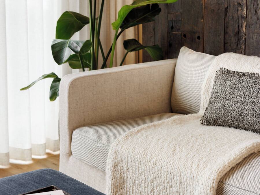 A living room with a sofa, a large plant, a wooden wall, and a window with curtains.