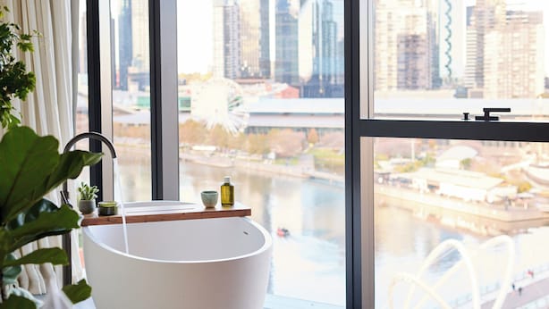 Een moderne badkamer met een groot bad, een raam met uitzicht op de stad en een potplant.