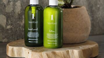 Two bottles of handwash and lotion from the brand '1 Hotel' on a wooden surface with a potted plant in the background.