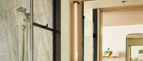 A modern bathroom with a glass-enclosed shower, a marble-tiled wall, a wooden vanity, and a large mirror.