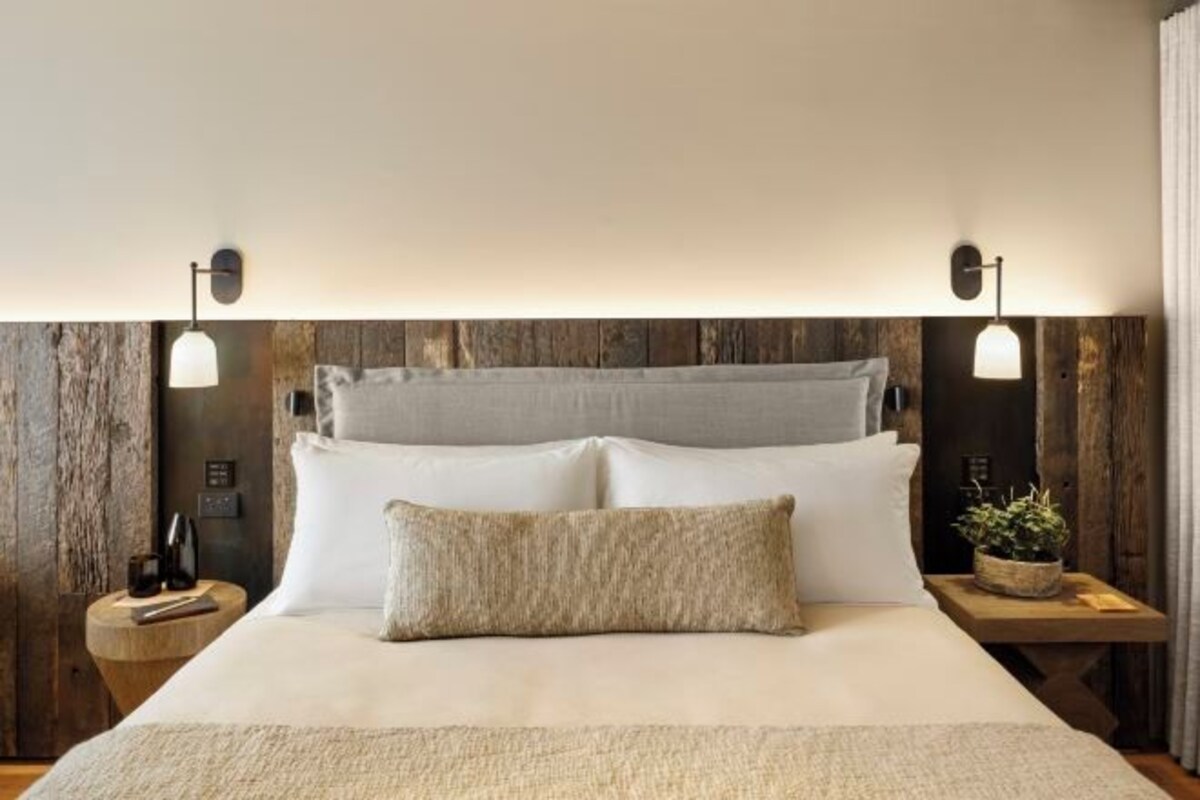 Una cama con sábanas blancas, un cabecero gris y dos mesitas de noche con lámparas.