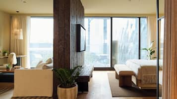 Een moderne hotelkamer met een groot raam, een flatscreen televisie, een bank, een bed en een potplant.