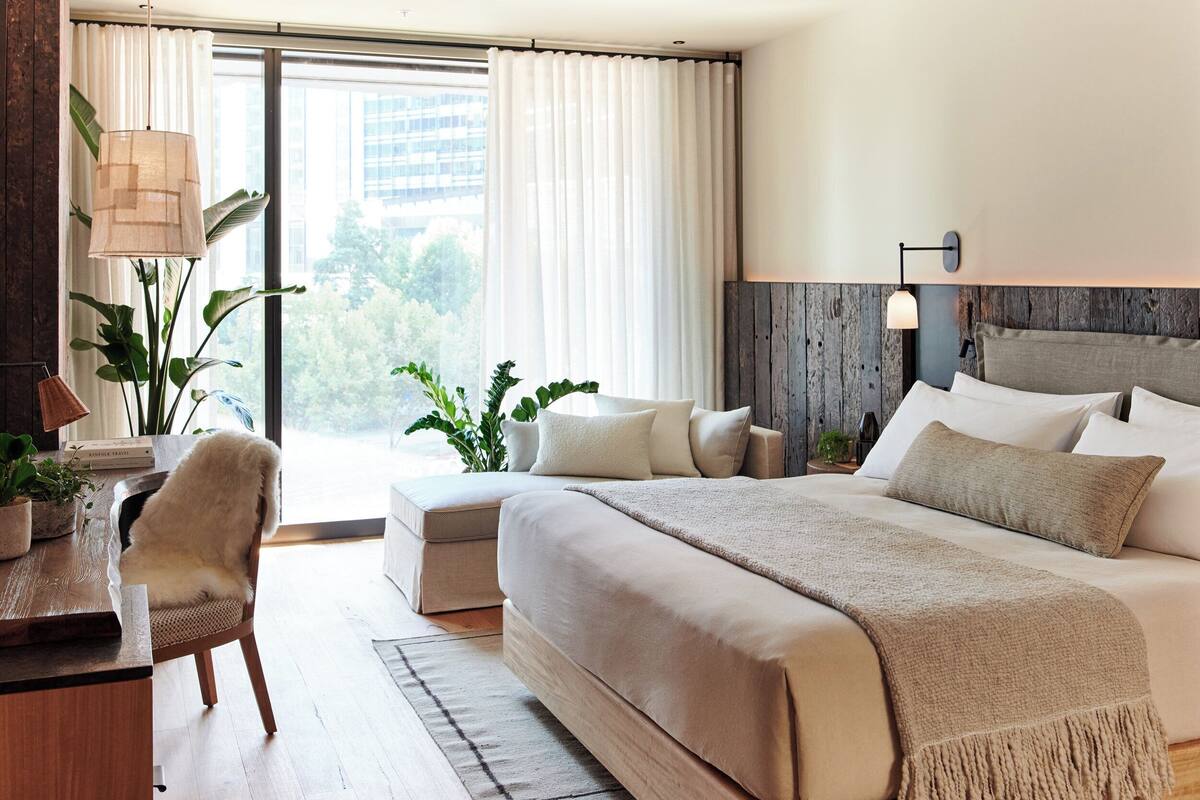 Habitación de hotel moderna con una cama grande, un escritorio, una silla y vistas al exterior.