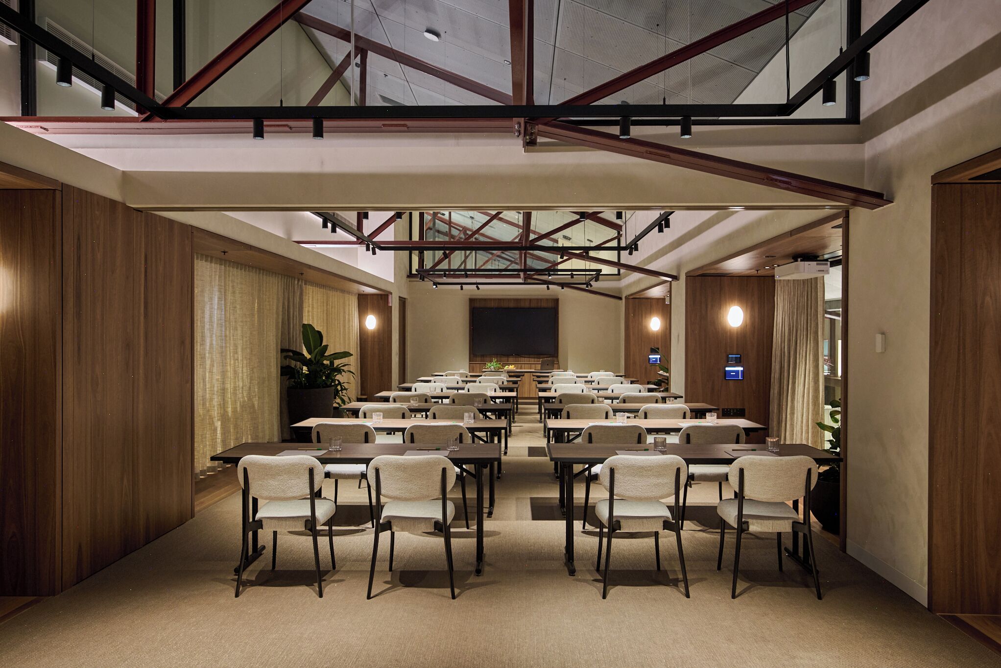 A conference room with a high ceiling, wooden paneling, and a large screen at the front.