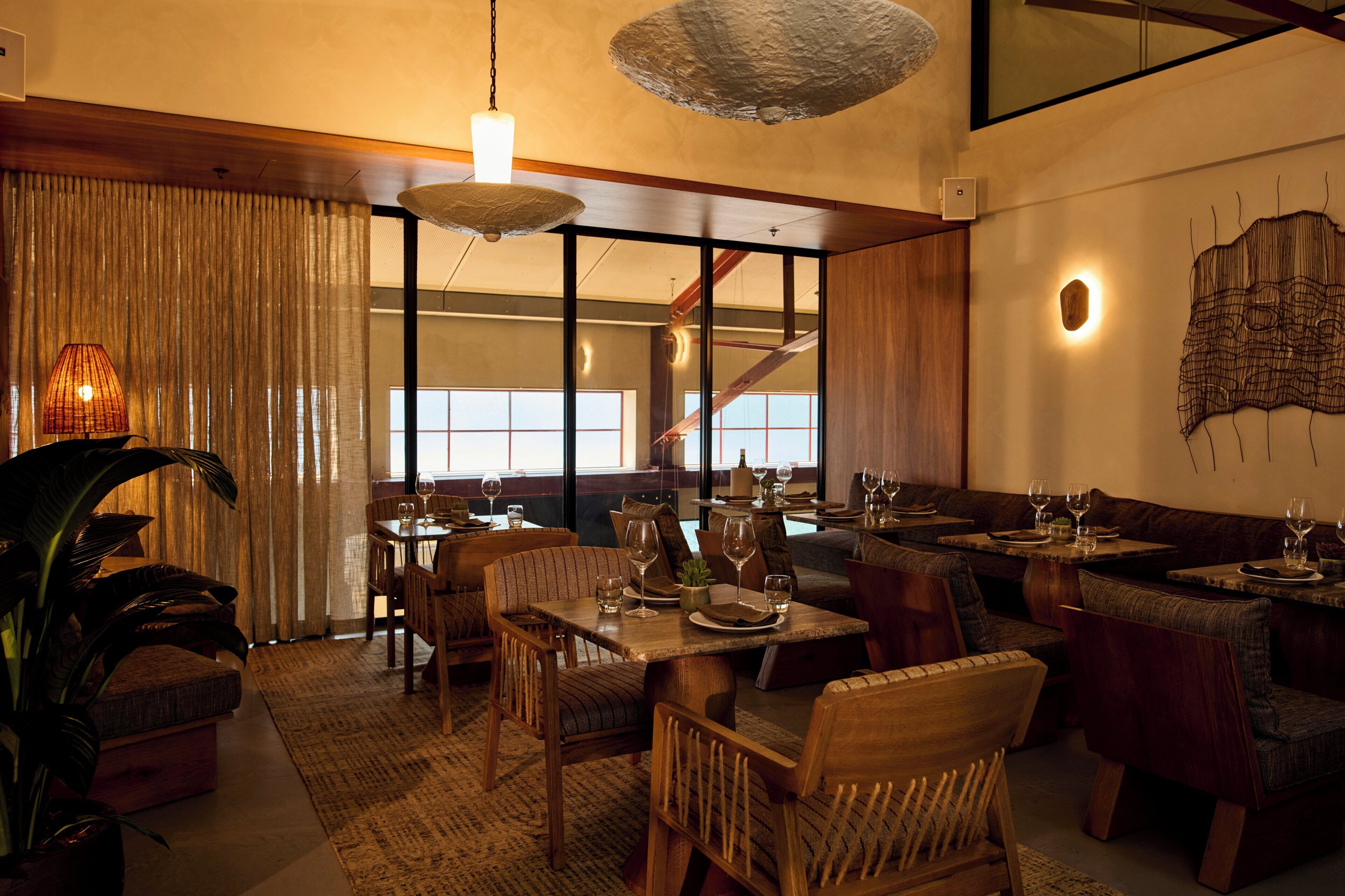 A restaurant with wooden furniture, a large plant, and a view of a staircase.