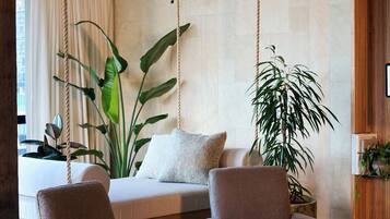 Une pièce comprenant un lit, deux fauteuils, une table basse et de grandes plantes.
