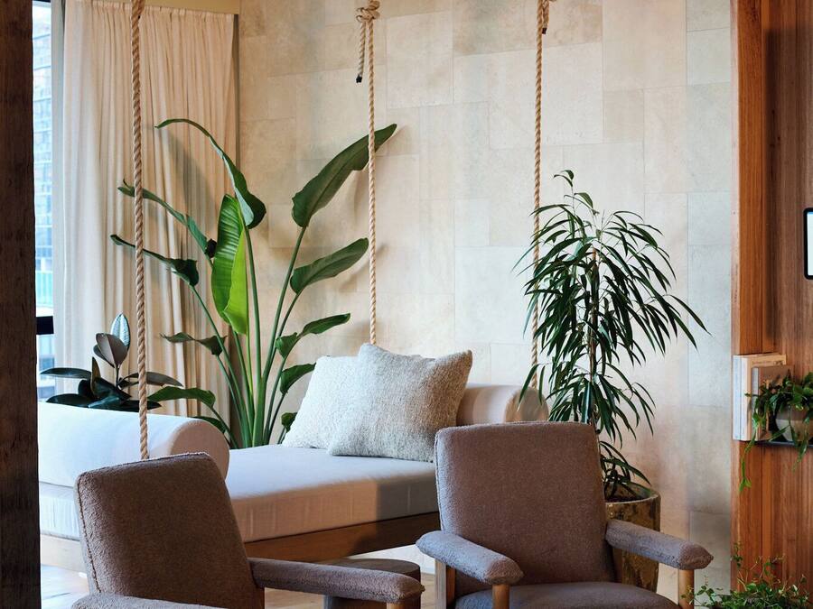 Une pièce comprenant un lit, deux fauteuils, une table basse et de grandes plantes.