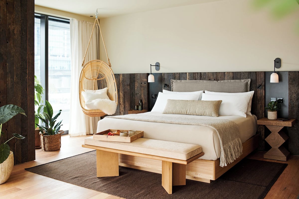 Un dormitorio moderno con una cama grande, una silla colgante, un banco de madera y vistas a la ciudad.