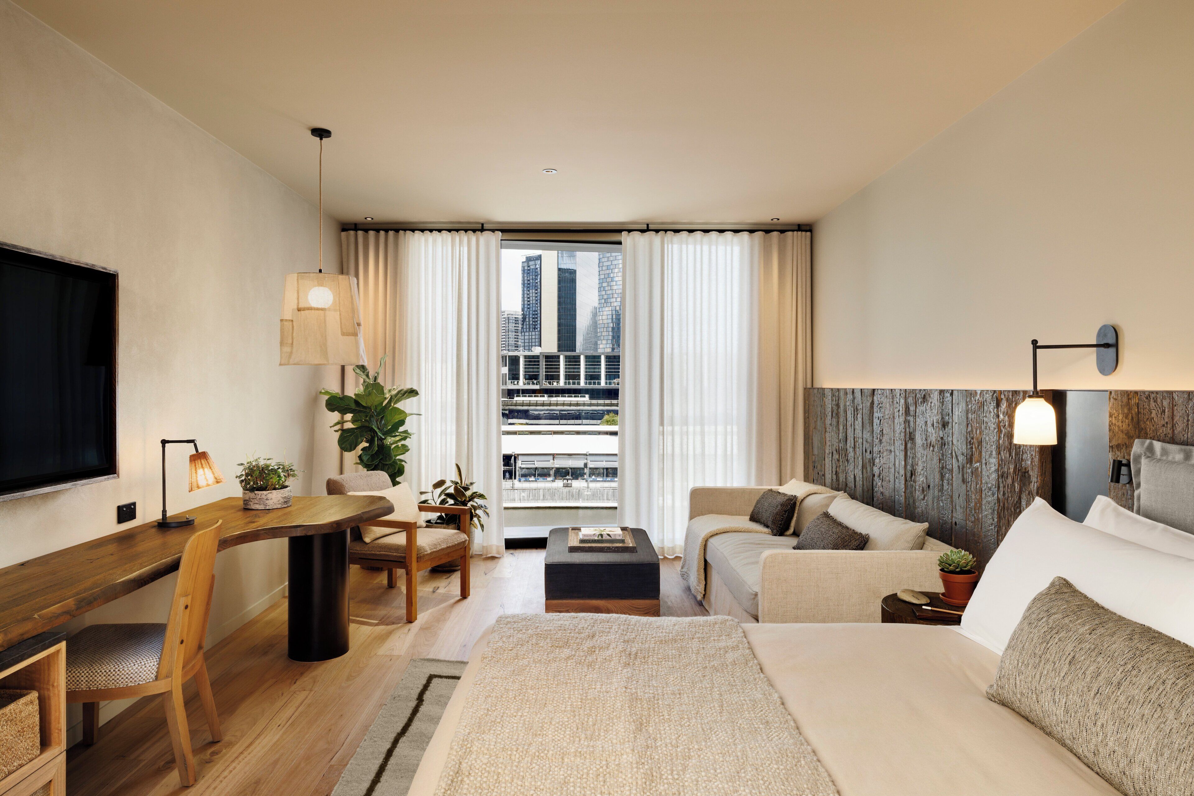 A modern hotel room with a large bed, a desk, a sofa, and a TV.