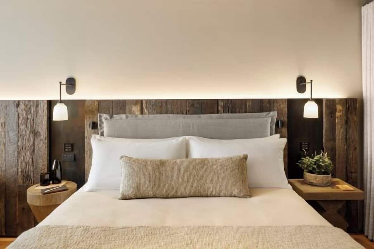 Una cama con sábanas blancas, un cabecero gris y dos mesitas de noche con lámparas.